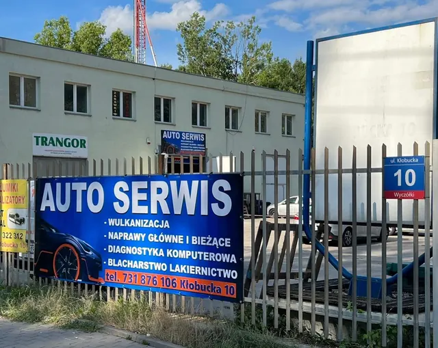 Wjazd: baner AUTO SERWIS na ogrodzeniu i niebieska tablica z numerem 10